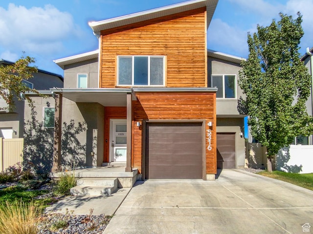 contemporary house with driveway, an attached garage, fence, and stucco siding