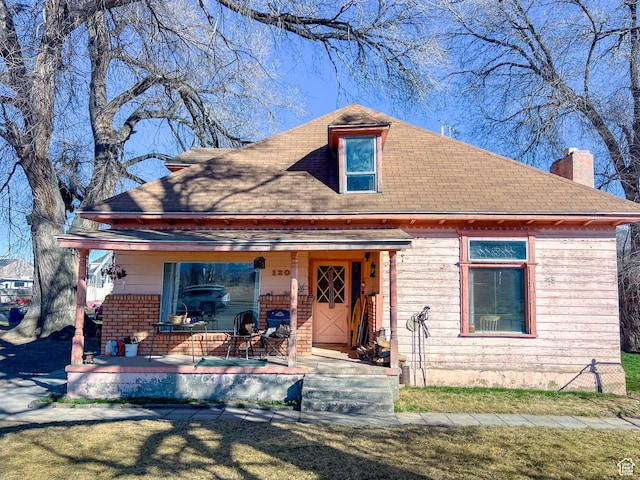 view of front of home with covered porch, a front lawn, and roof with shingles