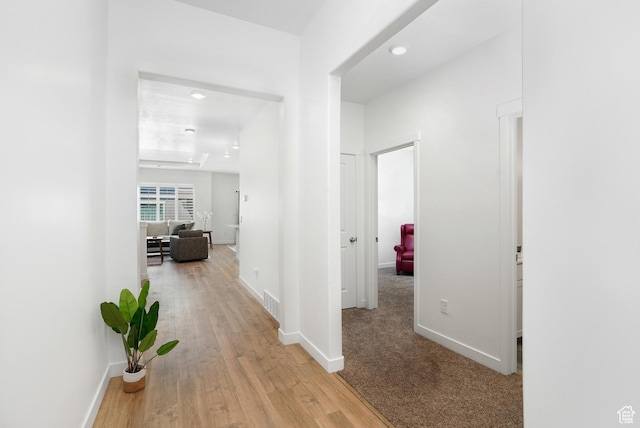 hallway featuring light wood finished floors, visible vents, and baseboards