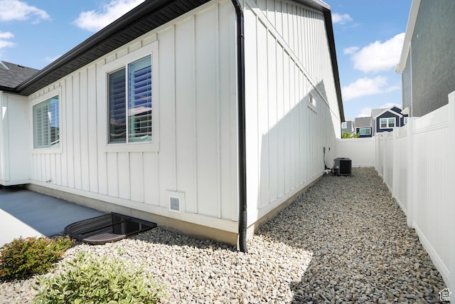 view of side of home with board and batten siding, a fenced backyard, and central AC