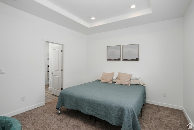 bedroom with carpet floors, a raised ceiling, and baseboards