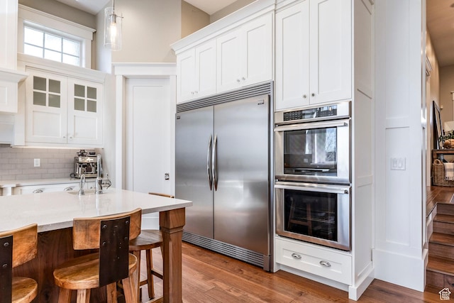 884 E Fence Post Rd S, Fruit Heights, UT 84037 - kitchen featuring appliances with stainless steel finishes, a kitchen breakfast bar, wood finished floors, white cabinetry, and backsplash