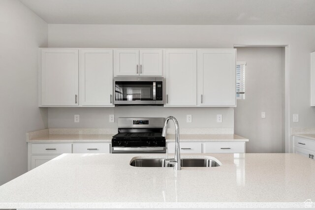 3537 S 3150 W Unit 106, West Haven, UT 84401 - kitchen featuring a sink, an island with sink, white cabinets, light stone countertops, and appliances with stainless steel finishes