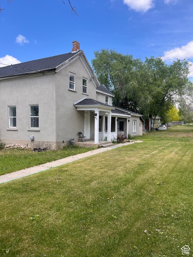 view of front of home featuring a porch, a chimney, stucco siding, a front yard, and roof with shingles
