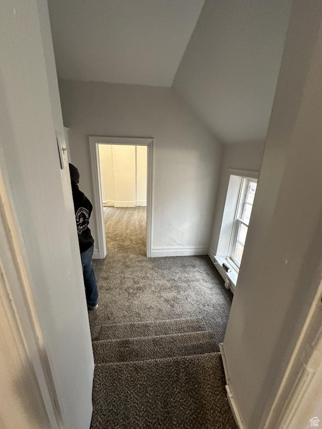 hallway with carpet floors, vaulted ceiling, and baseboards
