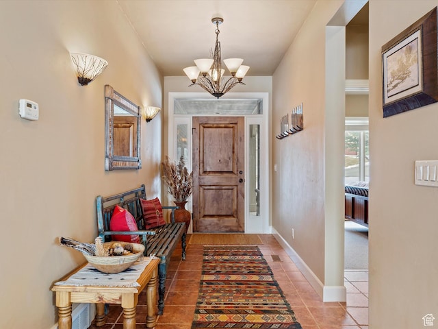 tiled entrance foyer featuring a chandelier and baseboards