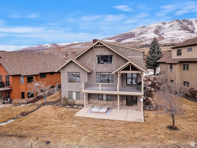 rear view of house featuring a patio area, stone siding, a mountain view, and a yard