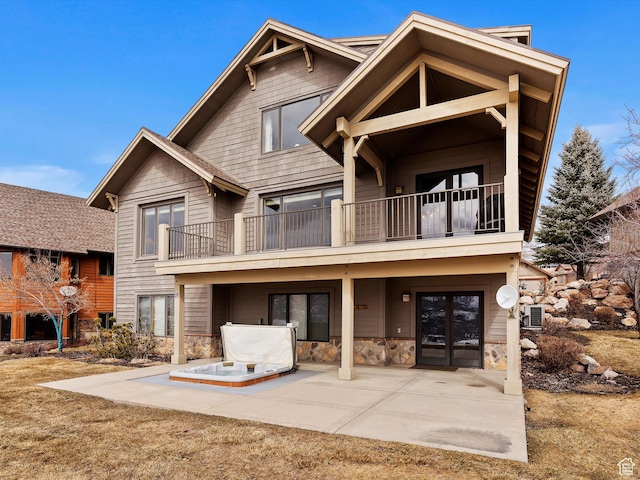 rear view of property featuring stone siding, a patio area, and a balcony