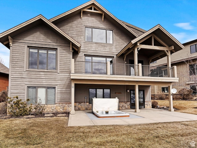 back of property featuring stone siding, a yard, a patio area, and a balcony