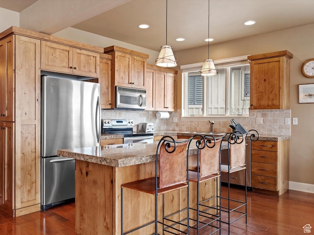 kitchen with dark wood-style floors, appliances with stainless steel finishes, a kitchen island, and tasteful backsplash
