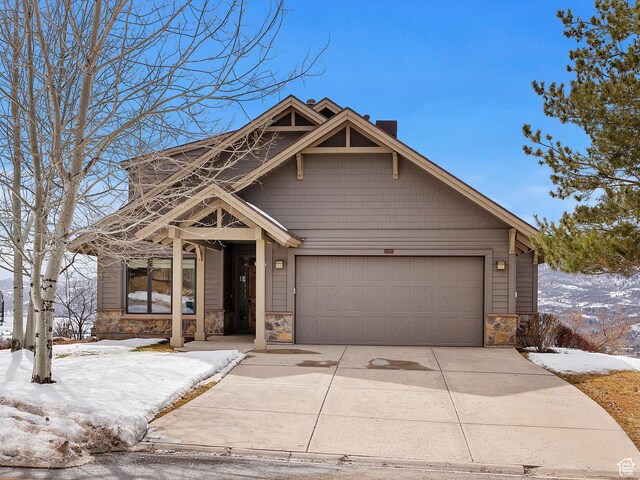 view of front of home with stone siding, an attached garage, a chimney, and concrete driveway