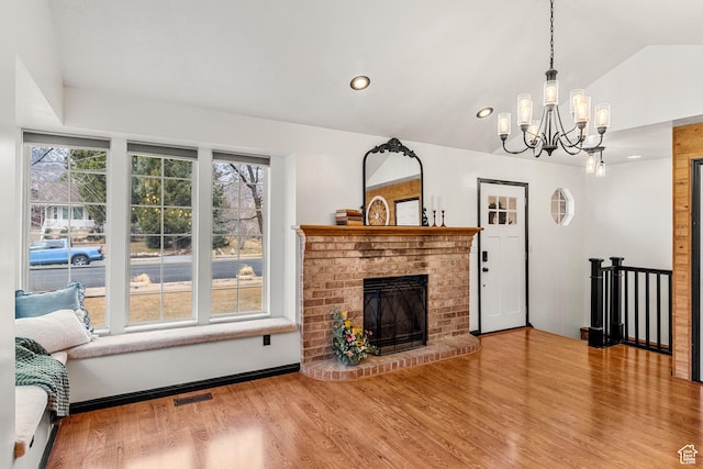 living area featuring a fireplace, visible vents, vaulted ceiling, wood finished floors, and a chandelier