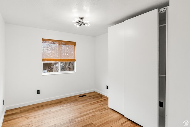 spare room with visible vents, light wood-style flooring, baseboards, and an inviting chandelier