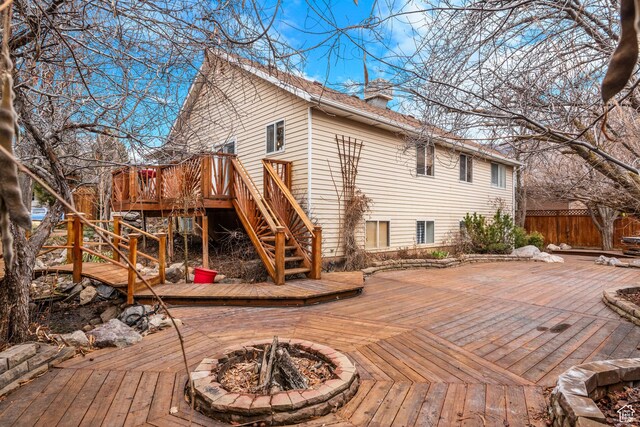 rear view of property with an outdoor fire pit, a chimney, a wooden deck, and fence