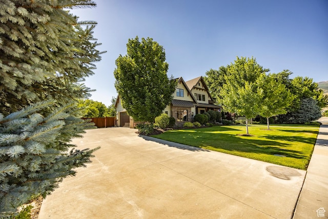 tudor home featuring concrete driveway, metal roof, a standing seam roof, fence, and a front yard