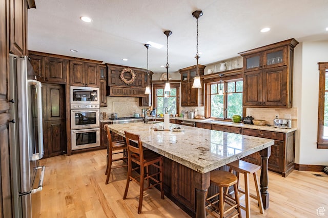 kitchen featuring light wood finished floors, a center island with sink, a breakfast bar area, stainless steel appliances, and backsplash