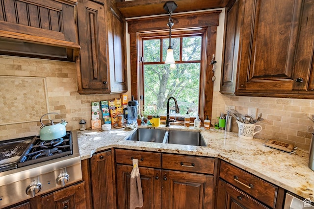 kitchen featuring stainless steel gas cooktop, light stone counters, a sink, and tasteful backsplash
