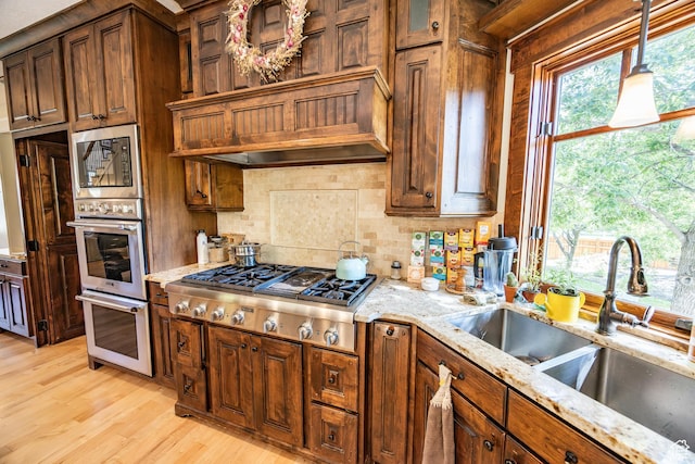 kitchen featuring appliances with stainless steel finishes, light stone countertops, custom exhaust hood, light wood-style floors, and a sink