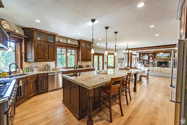 kitchen with appliances with stainless steel finishes, a sink, light wood-style flooring, and an island with sink