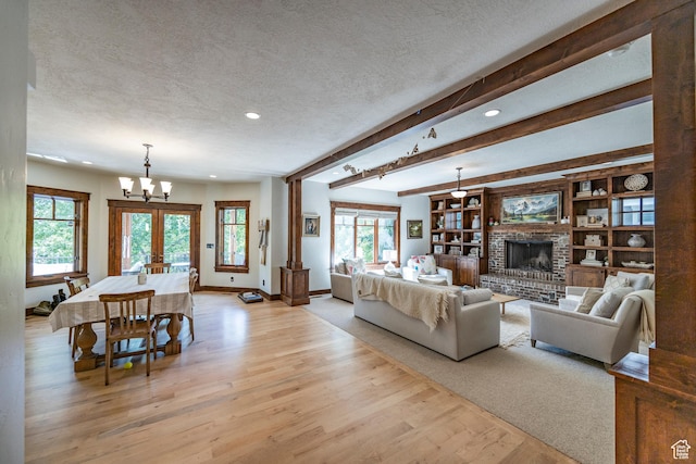 living room featuring beam ceiling, a fireplace, a textured ceiling, a chandelier, and light wood-type flooring