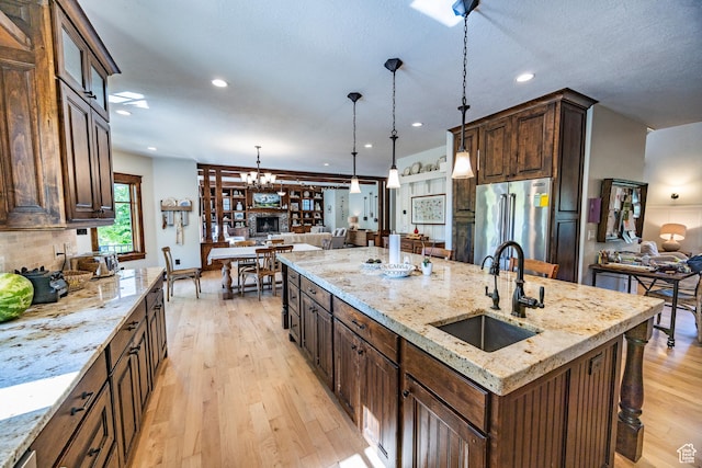 kitchen with light stone counters, pendant lighting, light wood finished floors, a sink, and high end refrigerator