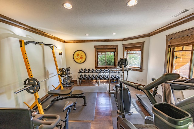 exercise area featuring visible vents, dark wood finished floors, a textured ceiling, and ornamental molding