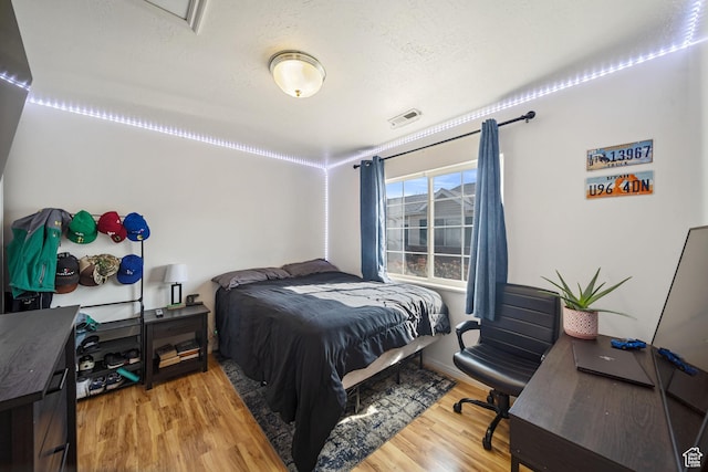 bedroom featuring visible vents, a textured ceiling, and wood finished floors