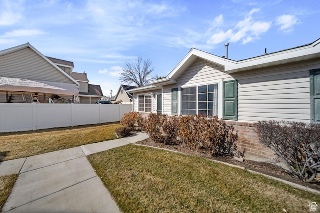 view of home's exterior with a yard, brick siding, and fence