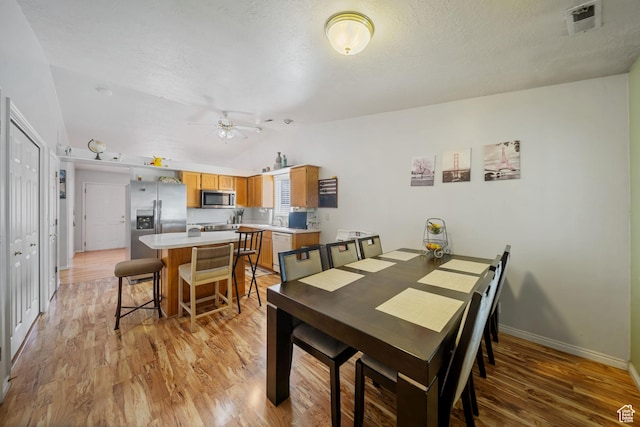 dining space with vaulted ceiling, ceiling fan, light wood-type flooring, and visible vents