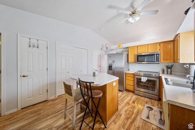 kitchen with lofted ceiling, a kitchen island, a sink, light wood-style floors, and appliances with stainless steel finishes