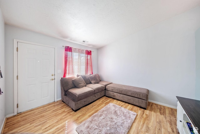 living room featuring a textured ceiling, baseboards, visible vents, and light wood-style floors