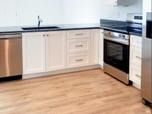 kitchen featuring dark countertops, white cabinetry, appliances with stainless steel finishes, and a sink