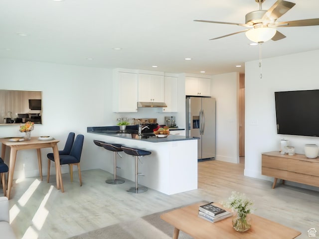 kitchen with a breakfast bar area, white cabinetry, a peninsula, stainless steel fridge, and under cabinet range hood