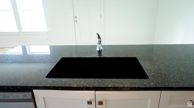 room details featuring dark stone counters, white cabinetry, a sink, and dishwasher