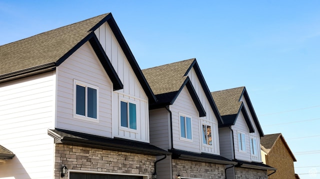 view of side of property with stone siding, board and batten siding, and roof with shingles