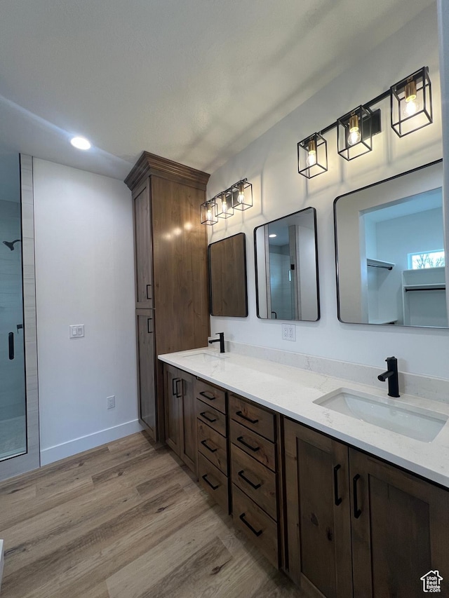 full bath featuring a sink, a shower with door, wood finished floors, double vanity, and baseboards