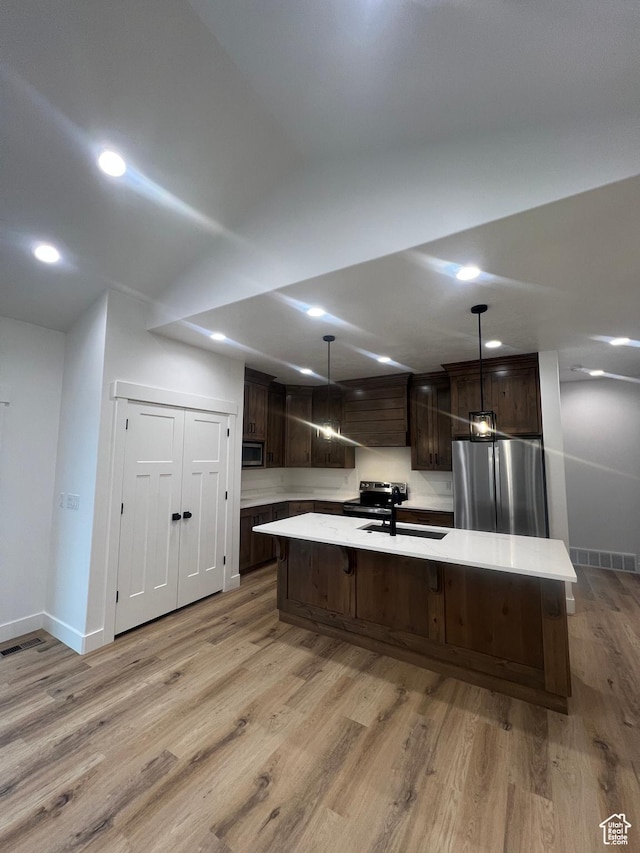kitchen featuring stainless steel appliances, light wood-style floors, light countertops, dark brown cabinets, and a large island with sink