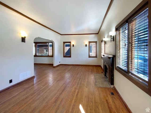 unfurnished living room with visible vents, arched walkways, baseboards, a fireplace with flush hearth, and light wood-style flooring