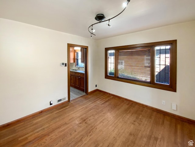 spare room featuring light wood-type flooring, a sink, visible vents, and baseboards