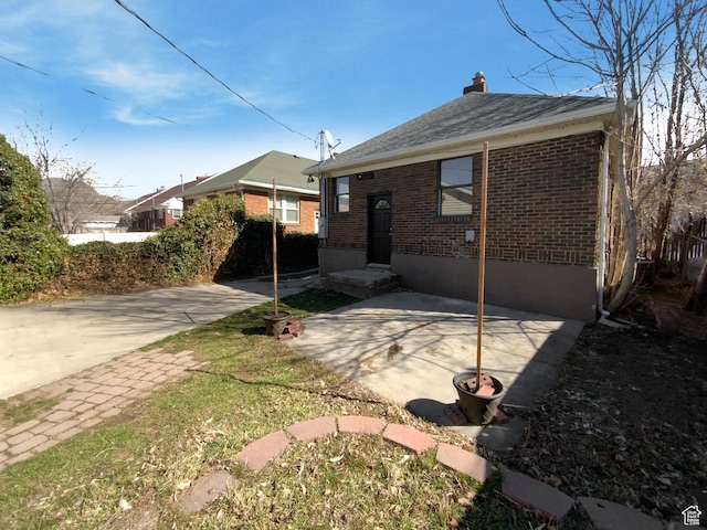 rear view of house with brick siding, a patio, and a chimney