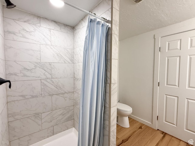 full bathroom with tiled shower, a textured ceiling, toilet, and wood finished floors