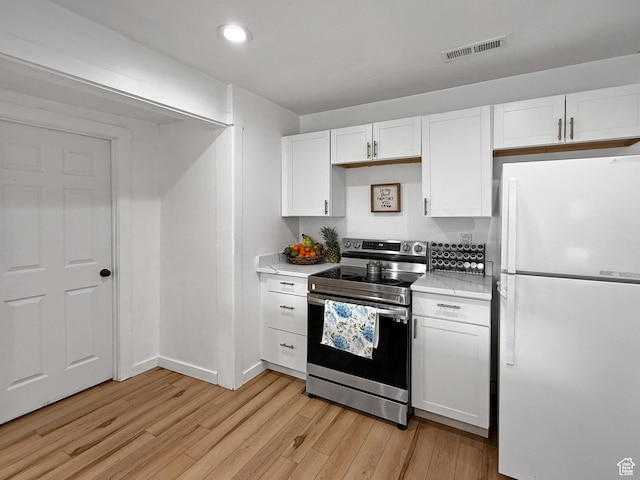 kitchen with electric range, visible vents, white cabinets, and freestanding refrigerator