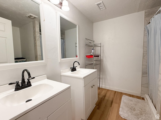 bathroom featuring a textured ceiling, wood finished floors, a sink, and visible vents
