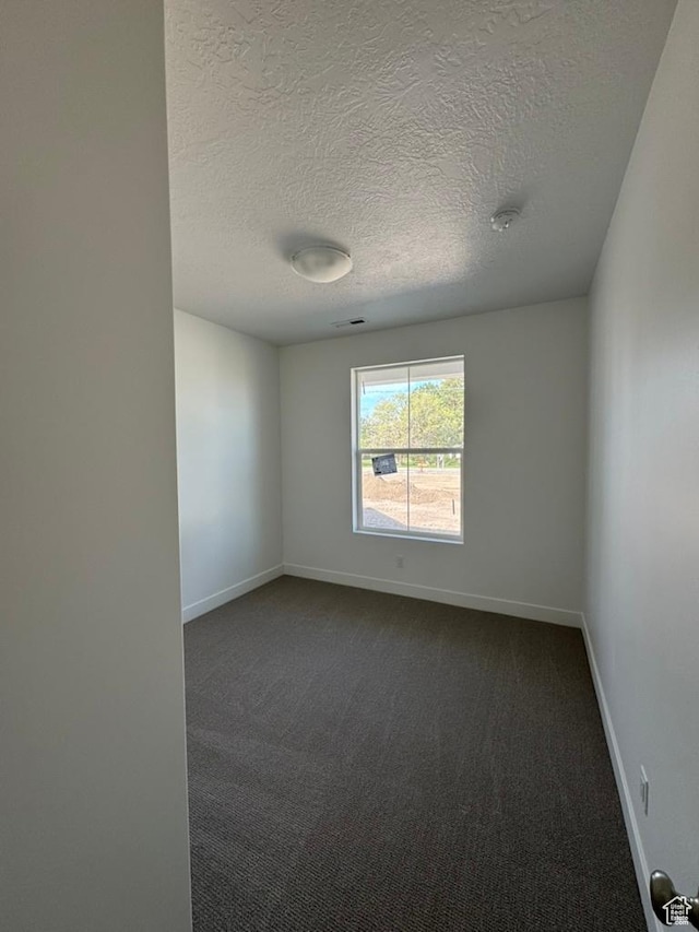 empty room featuring a textured ceiling, dark colored carpet, and baseboards