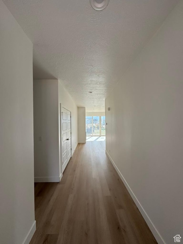 hall featuring baseboards, wood finished floors, and a textured ceiling