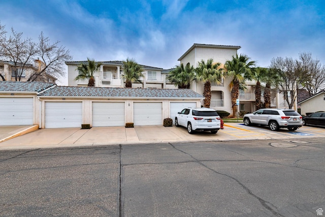 view of property with a tile roof, community garages, and stucco siding