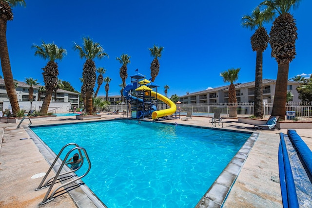 pool with a water slide, playground community, fence, and a patio