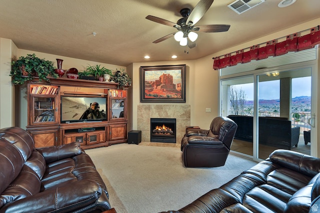 carpeted living area with ceiling fan, a fireplace, visible vents, and a textured ceiling