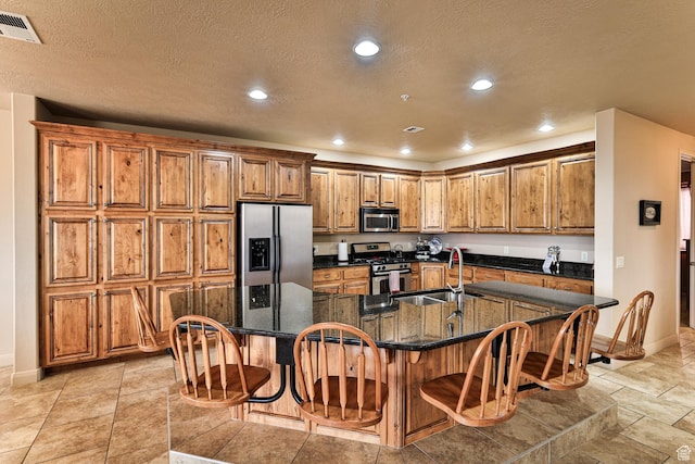 kitchen with stainless steel appliances, a sink, visible vents, a large island, and brown cabinets