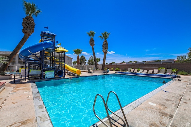 pool featuring a patio area, a water slide, playground community, and fence
